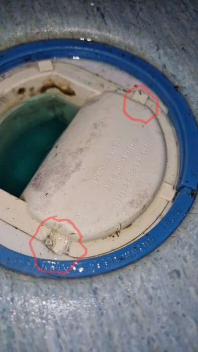 Bruten plastbit på övre sidan av en cirkulär lockmekanism, med spricka markerad i rött.