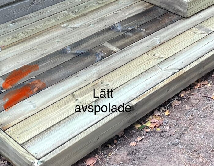 Trallvirke till entrétrapp i olika nyanser med två mörkare brädor och orange fläckar; texten "Lätt avspolade" syns på bilden.
