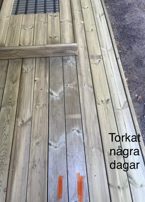Trägolv av tryckimpregnerat virke med två brädor som är märkbart mörkare än de andra. Markerat med orange tejp.