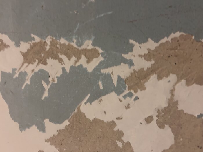 Flagad vägg med lager av blå och vit färg bortskrapade och blottad brun yta.