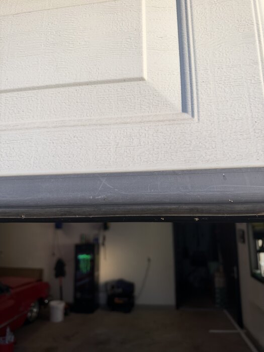 Närbild av bottenlisten på en vit garageport, suddig interiör av ett garage i bakgrunden.