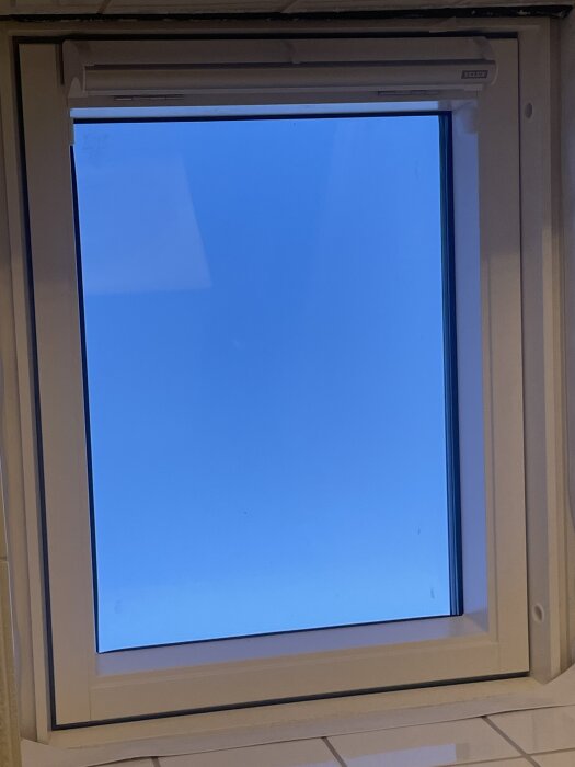 Veluxfönster utan lister, synlig tejp, skadat färg på trä, ljusblå himmel utanför.