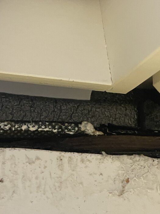 Detalj av fönsterinstallation där en skumkrage och tätningsmatta syns, med skador på färg och öppet trä som saknar lister.