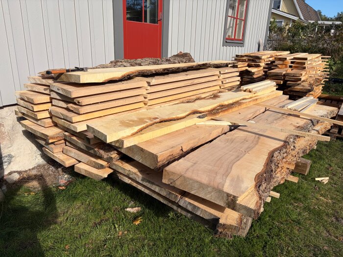 Staplade träplankor och "slabs" avsågade från ett stort träd ligger utanför en byggnad, redo att användas eller säljas som möbelvirke.