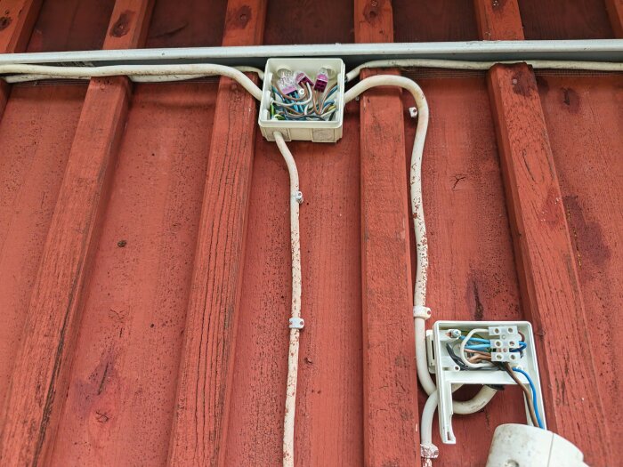 Trasig rörelsedetektor monterad på en röd trävägg med tre kopplade trådar synliga i kopplingsdosan.