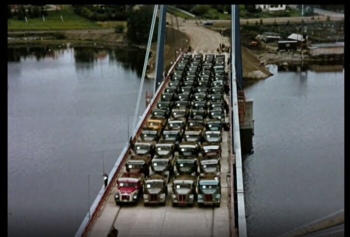 Bilden visar en bro med flera lastbilar parkerade på den, som tillsammans väger 816 ton. Bron omges av vatten och ett landskap.