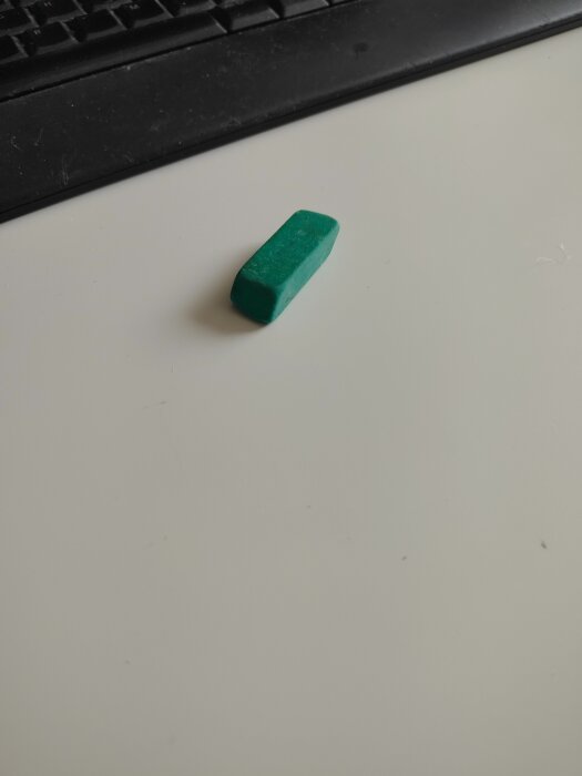 Grön suddgummi på ett vitt skrivbord bredvid ett tangentbord.