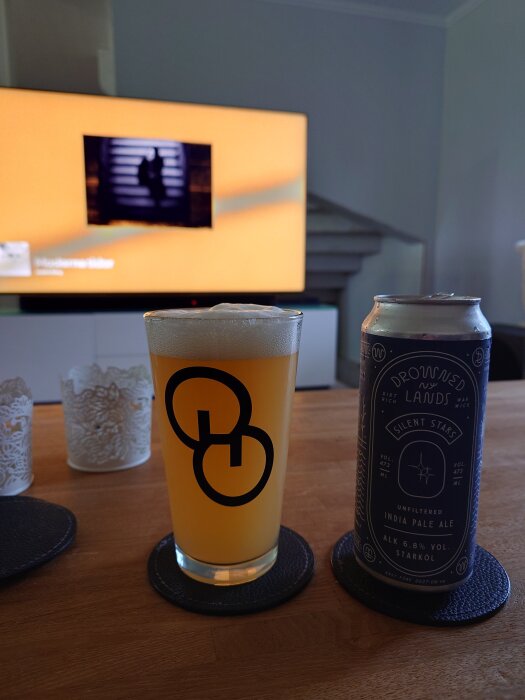 Ett glas med IPA från Drowned Lands och en ölburk står på ett bord framför en tv med orange skärm.