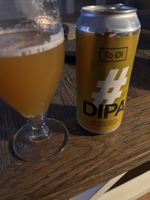 Ölglas med gyllene IPA och en gul DIPA-burk på ett träbord.