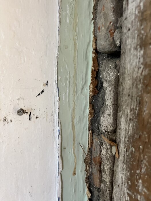 Vägg med lager av gammal ljusgrön färg, puts och brädor delvis avtäckt under renovering.