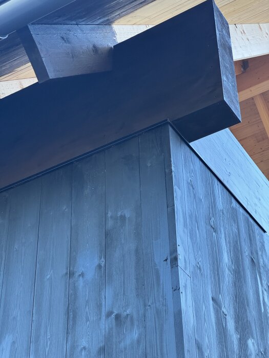 Byggnad med mörk panel och synliga bjälkar under ett tak, troligtvis som del av fasadarbete eller takinstallation på en fastighet.