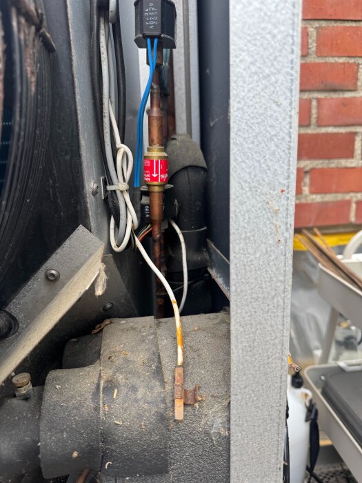 Köldmediegivare upphängd i kabel mot chassi, omgiven av isolerade ledningar och kretsar. Givaren verkar inte inkopplad i värmepumpens utedel.