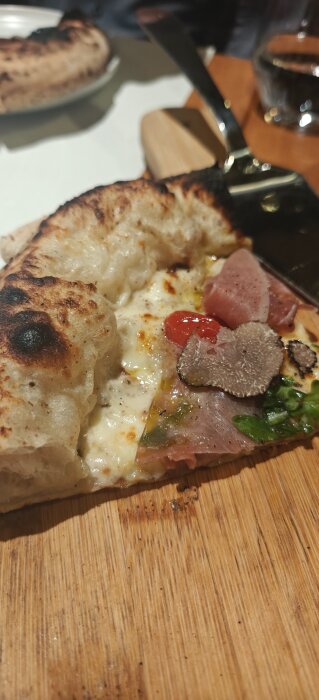 Pizza slice with truffle, prosciutto, and arugula on wooden board.