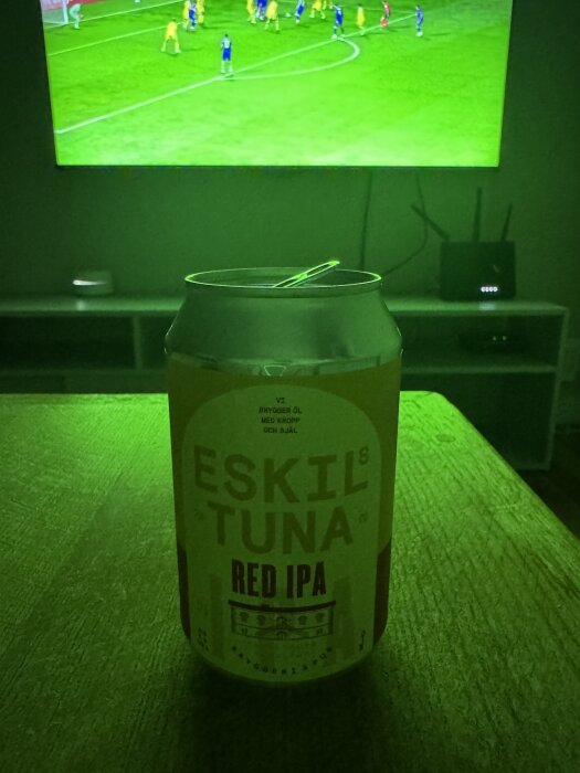 En burk Eskilstuna Red IPA står på bordet framför en TV som visar en fotbollsmatch.