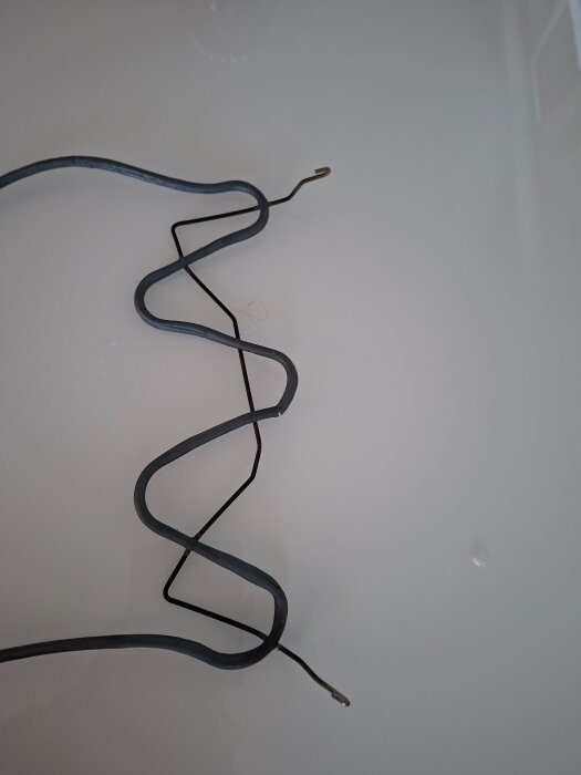 Två metallkrokar från ett element ligger på ett vitt underlag, krokarnas funktion är okänd enligt texten.