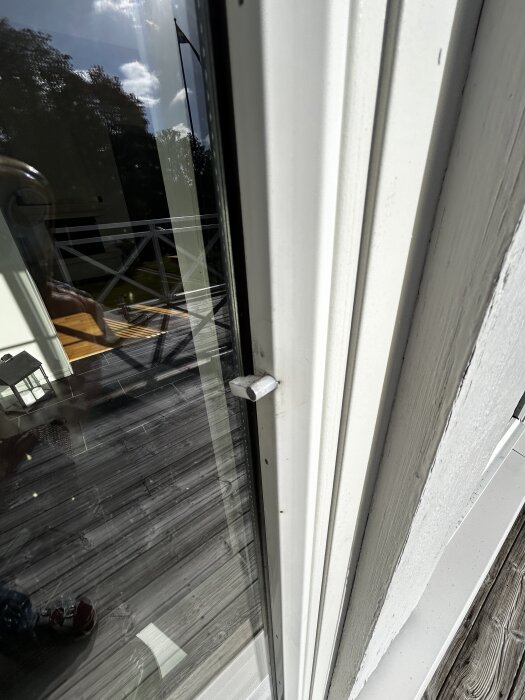 Närbild av ett 15 år gammalt elitfönster med en lös eller utsliten spröjslåsdetalj, ute på en träaltan i dagsljus.