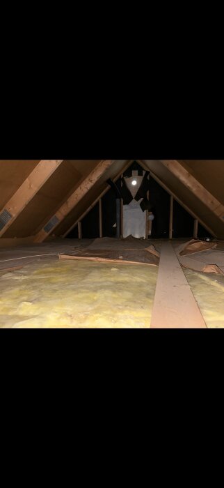Vindsutrymme med synliga takbjälkar, isolering och en rörledning i mitten, eventuell landgångsbyggnad planeras.