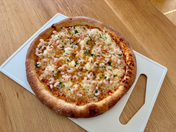 Fryspizza toppad med räkor och panko på en skärbräda.