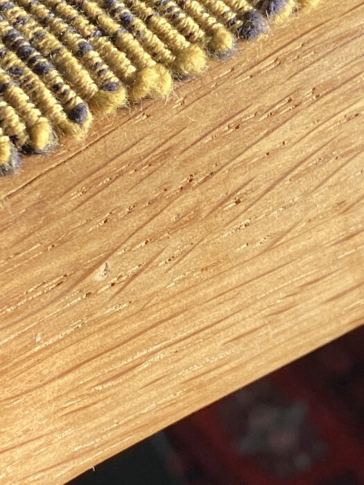 Närbild av ekbordets träytas struktur med en matta eller textil med gul och svart detaljering ovanpå.