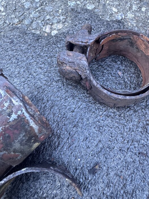 Rostiga metallringar med bult och mutter ligger på en asfaltsyta.