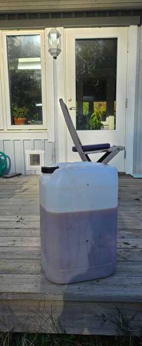 En plastdunk med äppelmust står på en trätrappa utomhus framför en glasdörr.