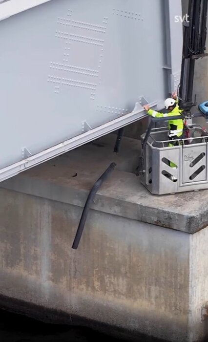 En person i varselkläder undersöker en brokonstruktion med en lyftkran, där en metallkonstruktion verkar ha förskjutits.