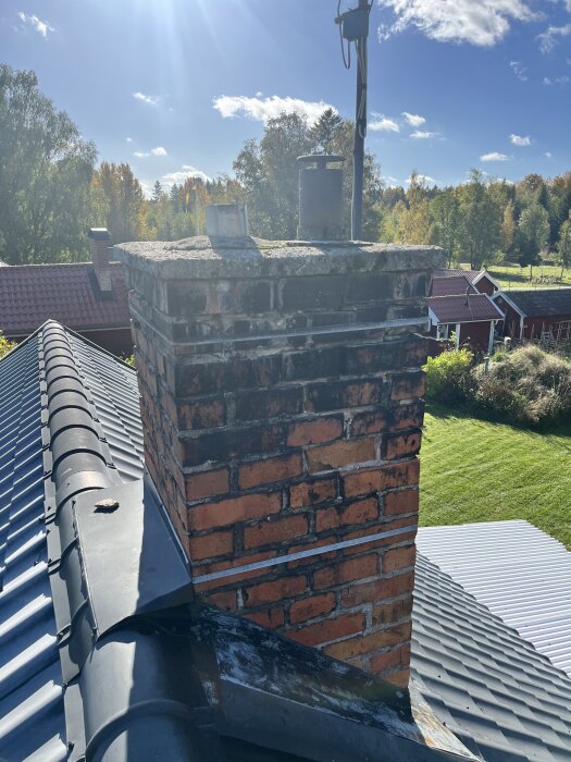 Tegelsten skorsten fotograferad från ett tak under en solig höstdag, omgiven av grönskande landskap och röda hus i bakgrunden.