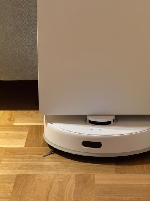 Sängbord monterat ovanför golv med robotdammsugare under på trägolv.