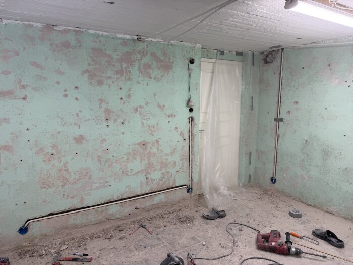 Elektriska dosor och rör i gröna stenväggar, spårade och bilade ur för elinstallation; verktyg och damm på golvet.