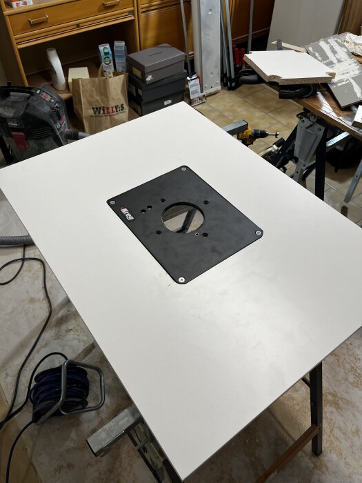 Fräsbord under uppbyggnad med skiva och infälld platta, omgivna av verktyg och byggmaterial.