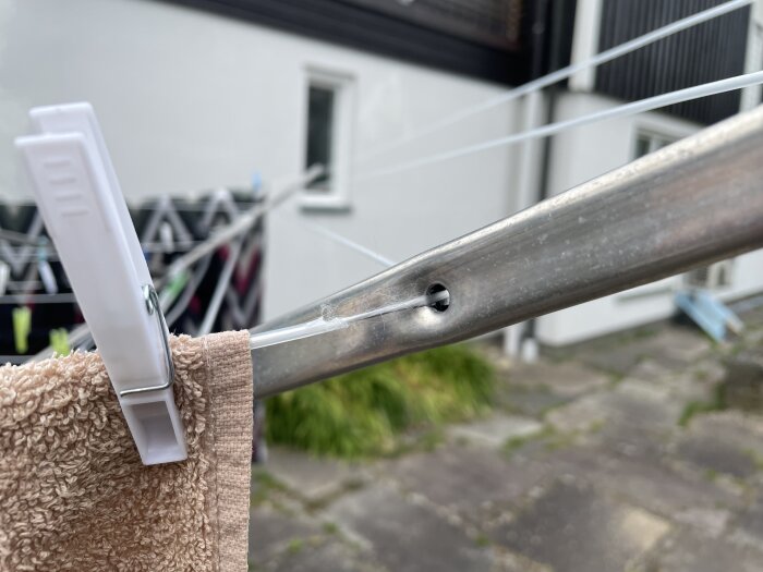 Sliten plastöverdragen tvättlina på tvättvinda med beige handduk fastklämd med plastklämma. Slitagemärke på linan syns tydligt.