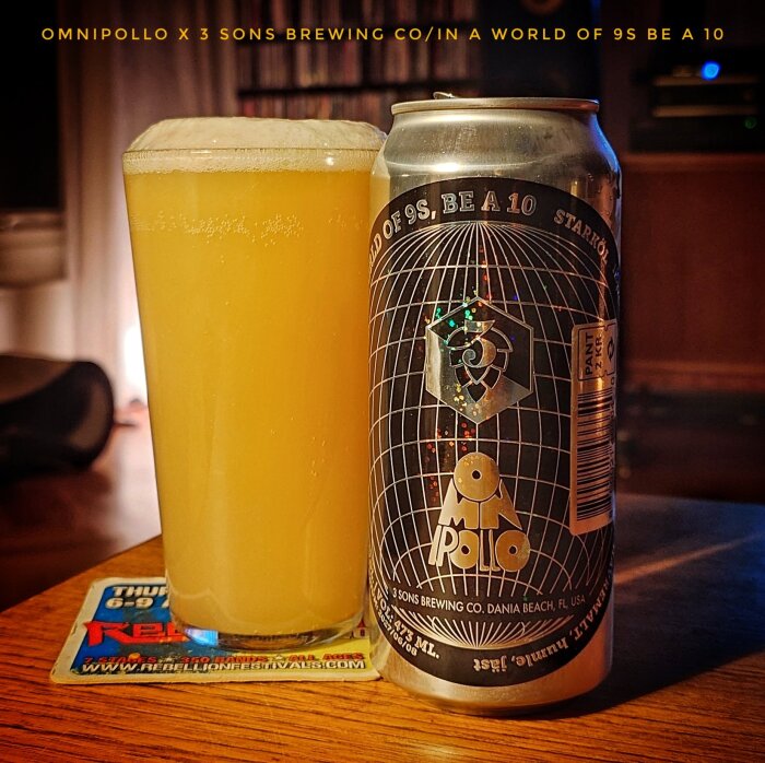 Ölglas med gul vätska och skummigt tak bredvid en burk från Omnipollo x 3 Sons Brewing Co. på ett underlägg.