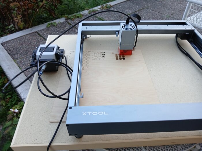 Lasergraveringsmaskin från XTool används för att gravera mönster på en träskiva utomhus.