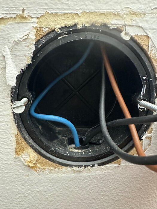 Elektrisk dosa med flera ledare, inklusive en blå ledare som går från eluttaget till lamputtaget, synliga kablar och gipsad vägg.