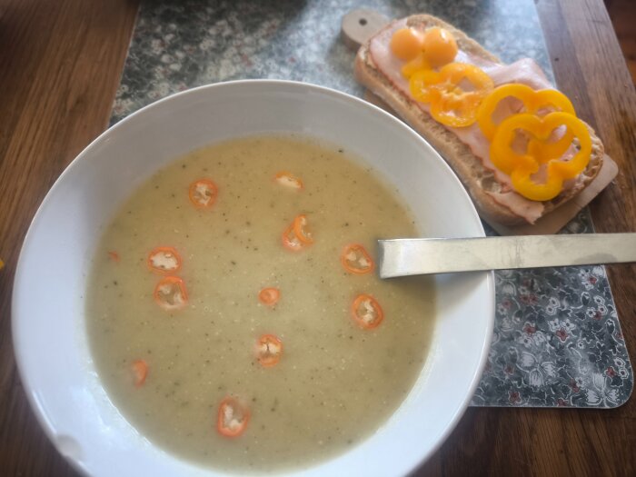 Potatis- och purjolökssoppa toppad med skivad chili, bredvid en ciabatta med grillad kycklingfilé och gul paprika.