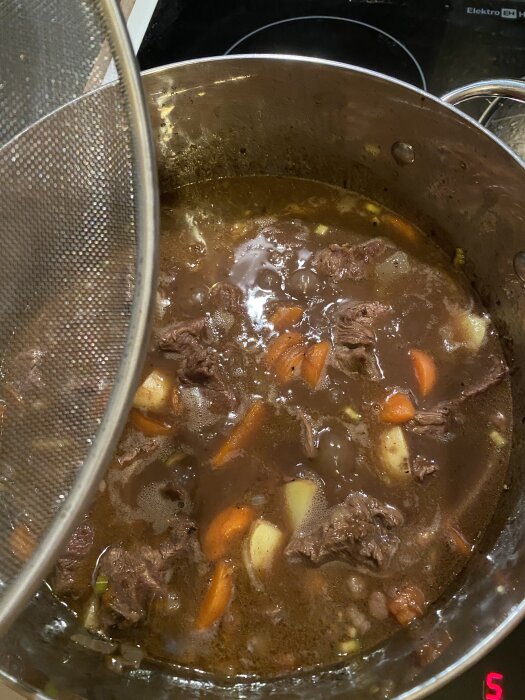 En kastrull med kalops, en köttgryta med köttbitar, morötter och potatis, puttrar på spisen.