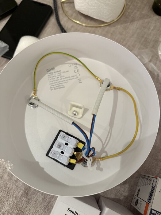 Takarmatur med ledningskopplingar och elektriska anslutningar synliga, på ett bord med verktyg och förpackningar i bakgrunden.