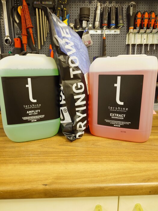 Flaskor med 5 liter Amplify Wet Coat och Extract Degreaser från Tershine, samt en ny torkduk, står på en arbetsbänk framför verktyg.