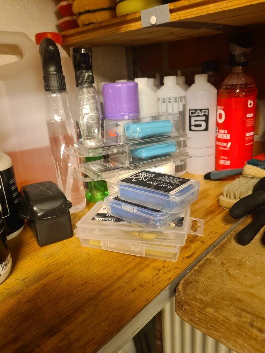 Bilvårdsprodukter på en hylla, inklusive sprayflaskor, rengöringsmedel och förpackningar med lera på en träbänk i ett garage.