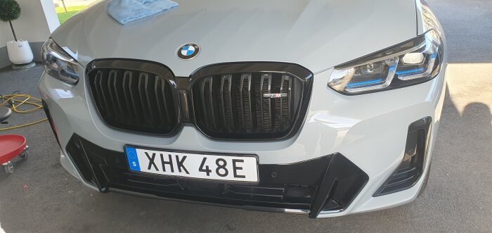 Främre delen av en BMW M i färgen Brooklyn Grey, med keramisk lackförsegling och mikrofiberduk på motorhuven. Registreringsskylt: XHK 48E.