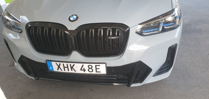 Framsidan av en silverfärgad BMW med registreringsnummer XHK 48E, fotograferad framifrån på en asfalterad yta.