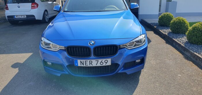 Blå BMW bil parkerad på asfalt med nummerplåt NER 769.