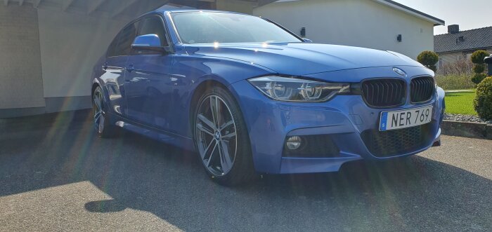Blå BMW parkerad framför ett hus, visar bilens design och rena yta under en solig dag.