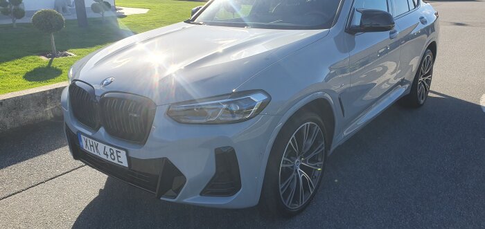 En nyligen handtvättad grå BMW parkerad på en solbelyst gata med reflektioner på karossen.