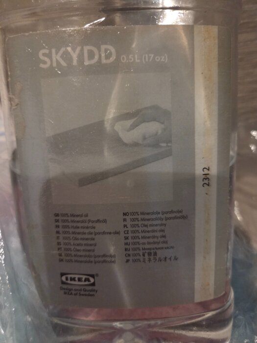 Flaska med 0,5L Skydd mineralolja från Ikea, etiketten visar en person som applicerar olja med en trasa på en yta.
