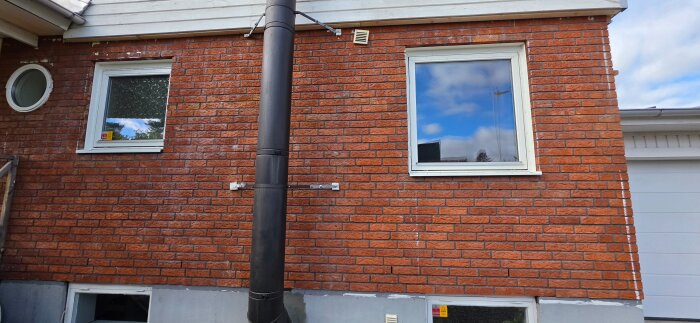 Tegelvägg med två fönster och ett rör samt detaljer som visar pågående renoveringsprojekt. Fönstren har flyttats in i fasaden.