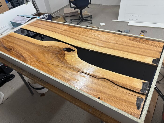 Bordsskiva av trä och epoxy, där epoxyn är i en fåra mellan två trästycken, färgad genomskinligt blågrå men ser svart ut på grund av underlaget.