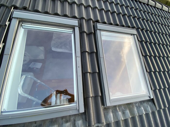 Två takfönster med svarta tegelpannor runt, visar del av interiör och stege reflekterat i glaset.