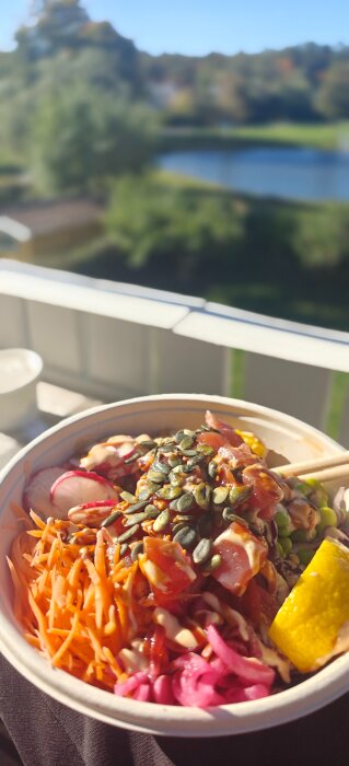 Skål med sallad innehållande pumpafrön, riven morot, inlagd rödlök, rädisor, och en citronskiva, fotograferad utomhus med suddig naturbakgrund.