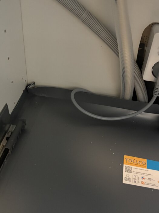 Under diskbänken med synliga vattenledningar och slarviga tätningar, plastmatta som inte når hela vägen bak och en etikett från Tollco.